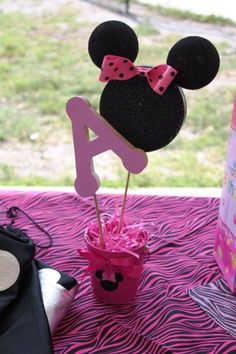 a minnie mouse cake topper on a pink and black tablecloth with a cupcake