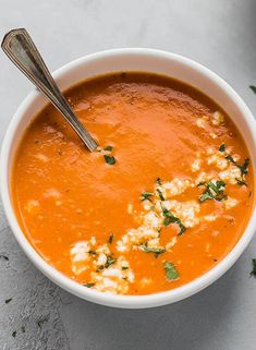 a white bowl filled with carrot soup and topped with parmesan cheese, fresh herbs and a spoon