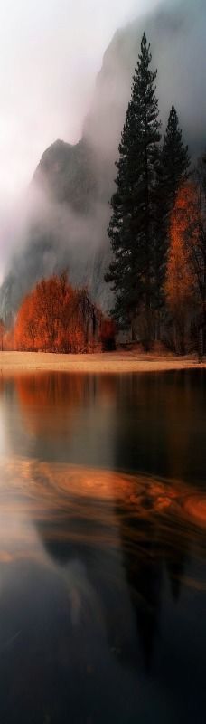 a lake surrounded by mountains and trees on a cloudy day with fog in the air