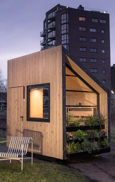 a small wooden building sitting on top of a lush green field next to a tall building