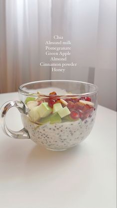 a glass bowl filled with fruit on top of a white table next to a window