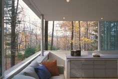 a kitchen and living room with large windows overlooking the woods in front of it,