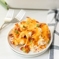 a white plate topped with macaroni and cheese covered in green onions next to a fork