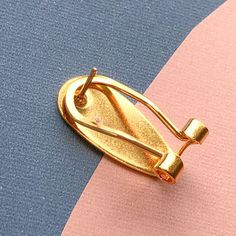 a gold colored pin sitting on top of a blue, pink and yellow striped surface