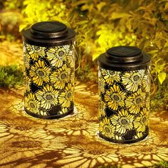 two yellow and black jars sitting on top of a patch of dirt next to grass