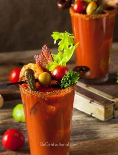 two glasses filled with different types of food and garnishes on top of a wooden table