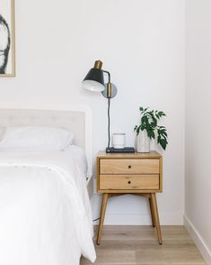 a bedroom with a bed, nightstand and plant on the side table in front of it