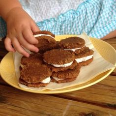 a child is reaching for some food on a yellow plate with white frosted marshmallows