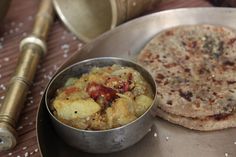 a metal plate topped with food next to a silver bowl filled with rice and bread