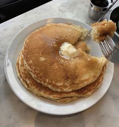 a stack of pancakes on a plate with butter and syrup being drizzled over them