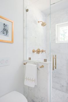 a white bathroom with marble walls and gold fixtures on the shower head, toilet seat cover, and towel rack