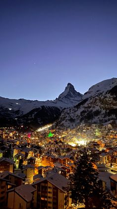 the city lights are lit up at night in the snow covered mountains behind it is a snowy mountain range