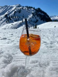 a glass filled with liquid sitting on top of a snow covered ground next to a mountain