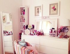 a white dresser topped with lots of drawers next to a wall filled with framed pictures