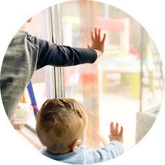 a young boy looking out the window at another child holding his hand up in front of him