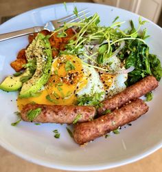 a white plate topped with sausages, avocado and an egg on top