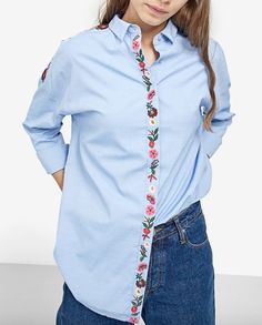 a woman with her hands on her hips wearing a blue shirt and floral neck tie