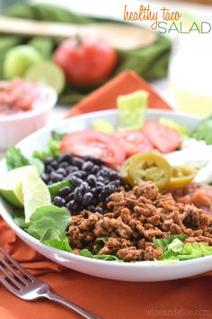 a white bowl filled with lettuce, black beans and tomatoes next to a fork