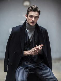 a man sitting on top of a stool wearing a suit and turtle neck sweater with pinstripe pants