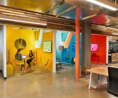 a woman sitting at a desk in an office with brightly colored walls and chairs around her