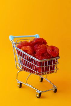 a miniature shopping cart filled with strawberries on an orange background