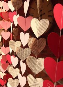 many heart shaped paper hanging from strings on a wall with a clock in the background