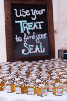 jars of honey sit on a table with a sign in the background that says use your treat to find your seat