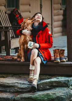 a woman is sitting on the steps with her dog and drinking from a coffee cup