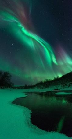 an aurora bore is seen in the night sky over a frozen lake and snow covered ground