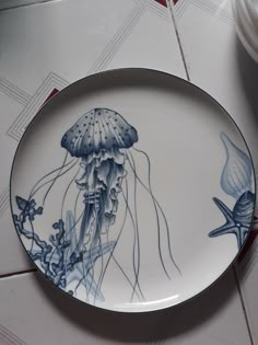 a blue and white plate with an image of jellyfish on the side, sitting on a tile floor