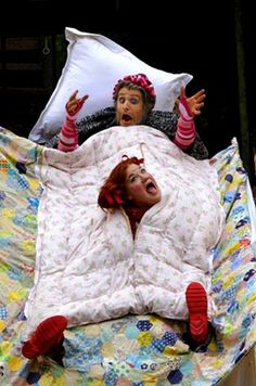 two women laying on top of a bed covered in blankets and pillows with their mouths open