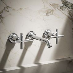 two chrome faucets on the wall in a bathroom with marble walls and flooring