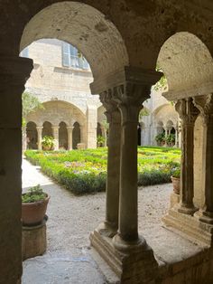 an outdoor courtyard with stone pillars and flowers in the center, surrounded by greenery