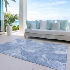 a living room with a couch, rug and large window overlooking the ocean on a sunny day