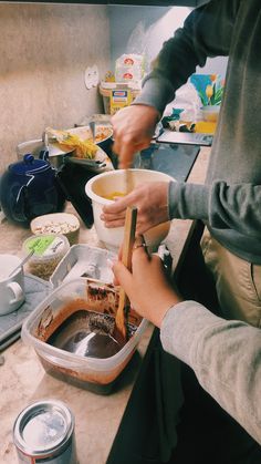 two people preparing food in a kitchen with bowls and spoons on the counter top