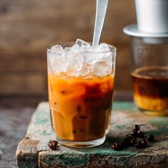 an iced beverage in a glass with ice and coffee beans on the table next to it