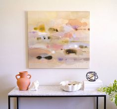 a painting on the wall above a table with vases