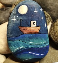 a painted rock with a boat in the ocean on it's side next to some rocks