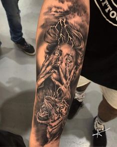 a man with a black and white tattoo on his arm is holding a tiger in front of him