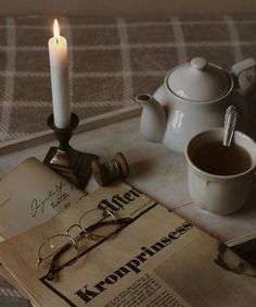 an open book with glasses on it next to a cup of coffee and a candle