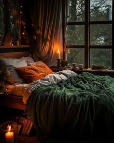 an unmade bed in a dark room with candles on the window sill and curtains