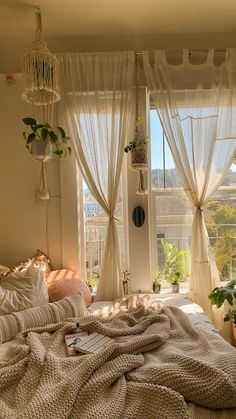 an unmade bed in front of two windows with curtains and plants on the window sill