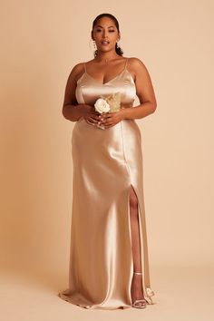 a woman in a gold gown holding a flower and posing for the camera with her hands on her hips