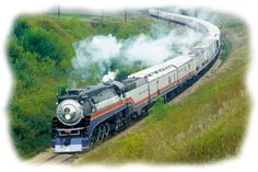 a train is traveling down the tracks near some trees and grass with steam pouring out of it