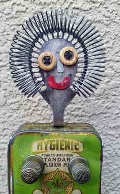 an old tin can with a weird looking face on it's head and hair