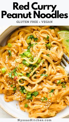 red curry peanut noodles in a white bowl with a fork and lime wedge on the side