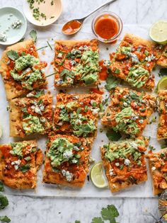 several pieces of flat bread topped with guacamole and other toppings on a cutting board