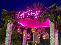 the entrance to a party with lights and lanterns on it's pillars, surrounded by palm trees