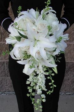 a bouquet of white flowers is being held by a woman in a black dress on the street