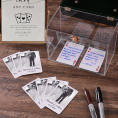 four playing cards in a clear case next to an empty card box and pen on a wooden table